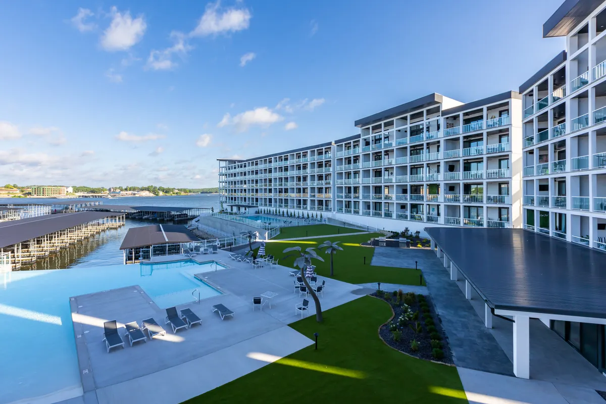 A modern exterior shot capturing a swimming pool framed by contemporary architecture, a landscaped garden, and a nearby dock area. The scene is upscale and relaxed, with inviting spaces for sunbathing, socializing, and water activities, all set against a sunset sky.