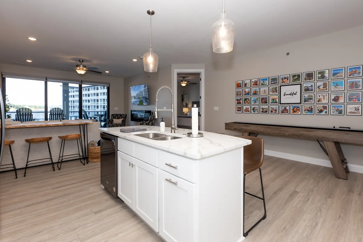 An inviting kitchen with a comfortable bar seating area and a gallery wall of family photos in the background. The space is set up for socializing, with a warm, lived-in feel that emphasizes togetherness over meals.