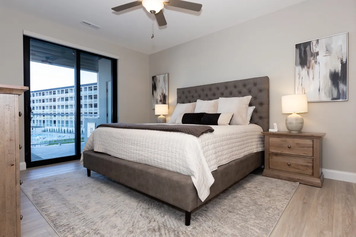 This image features a serene bedroom with a comfortable bed as the focal point, complemented by a nightstand, window, and tasteful artwork. Soft natural light streams through the window, creating a tranquil and cozy atmosphere ideal for unwinding or reading.