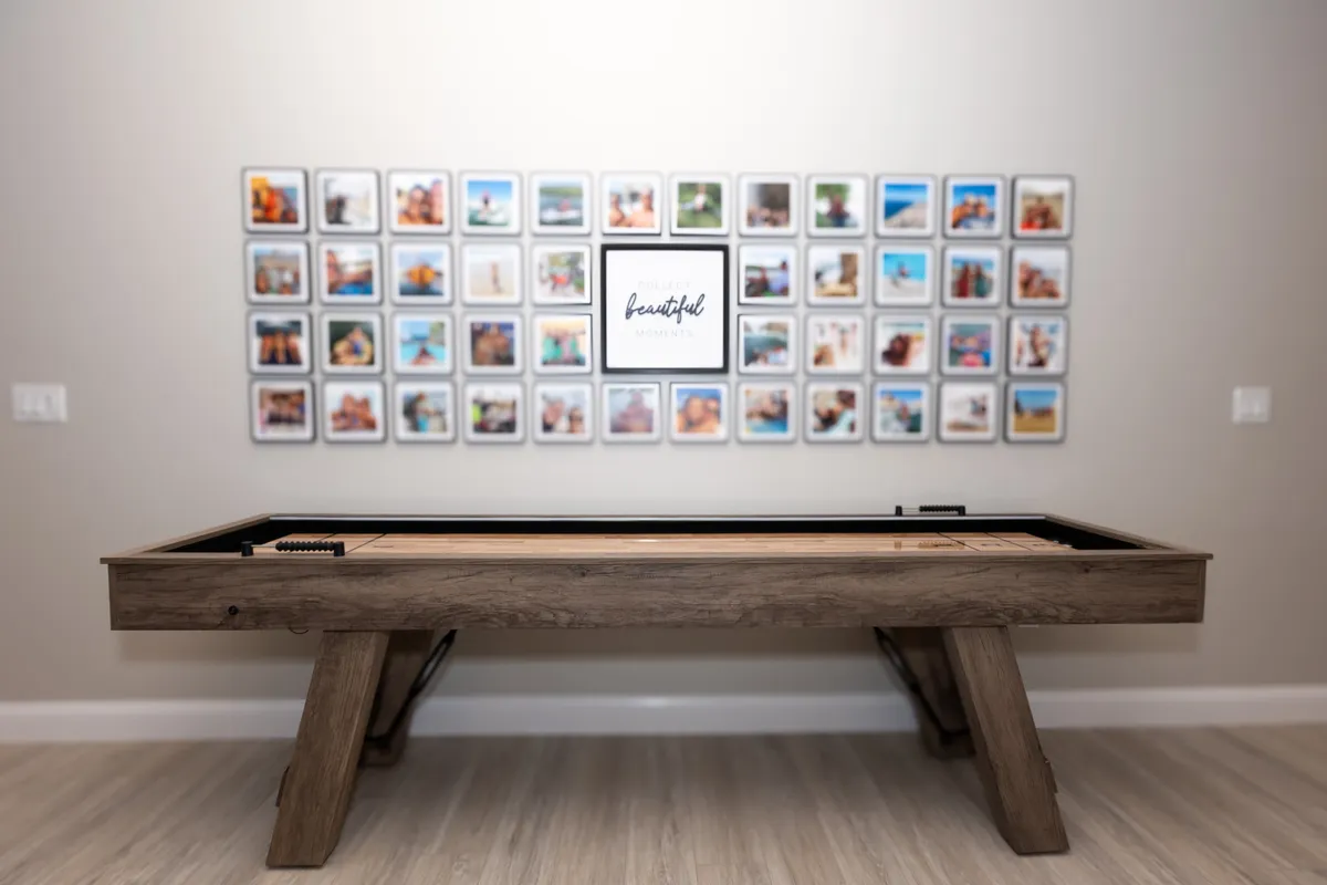 This interior image showcases a shuffleboard table situated in a spacious, well-lit room adorned with a photo wall. The setting is vibrant and inviting, with ample space for socializing and group activities. The presence of family photos hints at gatherings and memorable occasions, perfectly aligning with the idea of entertainment within the condo.