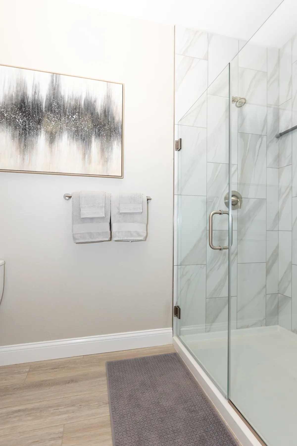 A tranquil bathroom featuring a glass shower, soft towels, and wall art. The setting is refined and calming, offering a quiet space for self-care and relaxation.