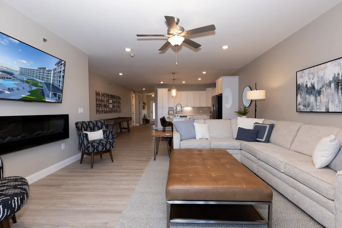 A cozy, open-concept living area with a large sectional sofa faces a wall-mounted television above a modern fireplace. The space is styled for comfort and conversation, featuring decorative wall art and a modern coffee table, suggesting it’s ideal for relaxing or hosting game nights and group meals.