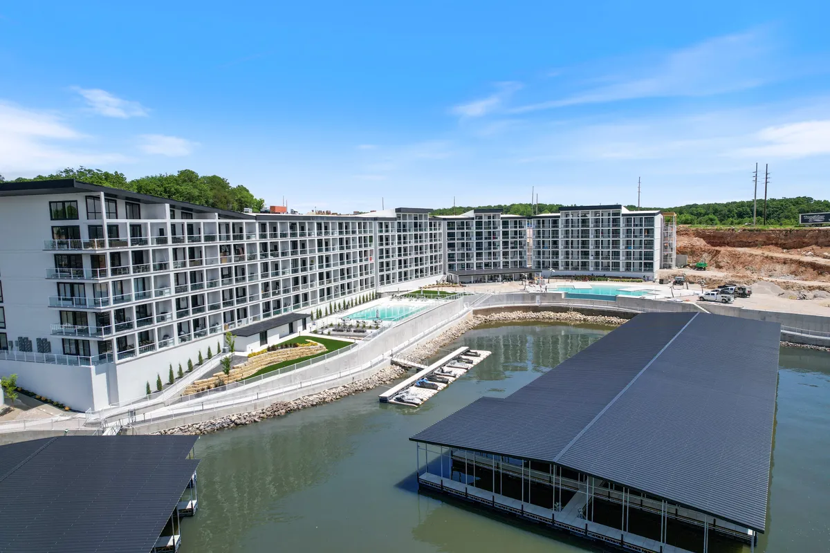 A wide exterior shot featuring modern architecture, two swimming pools, a marina with boats, and lush green landscaping. The scene is lively yet relaxed, offering a taste of both water-based adventure and luxurious leisure.