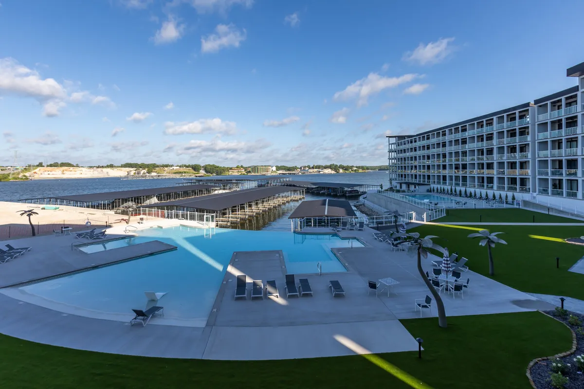 The scene features an inviting infinity pool overlooking boating docks, with the hotel building and landscaped outdoor space providing a resort-like atmosphere. The water, docks, and pool are all in clear view, suggesting a seamless transition from leisure to adventure.